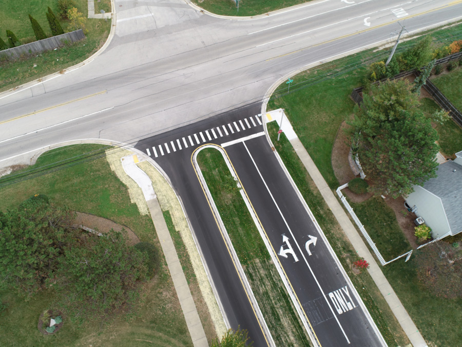 Hook-Orchard-DJI_0472 Aerial view of a newly constructed road intersection featuring turn lanes, freshly painted markings, and surrounding green spaces.