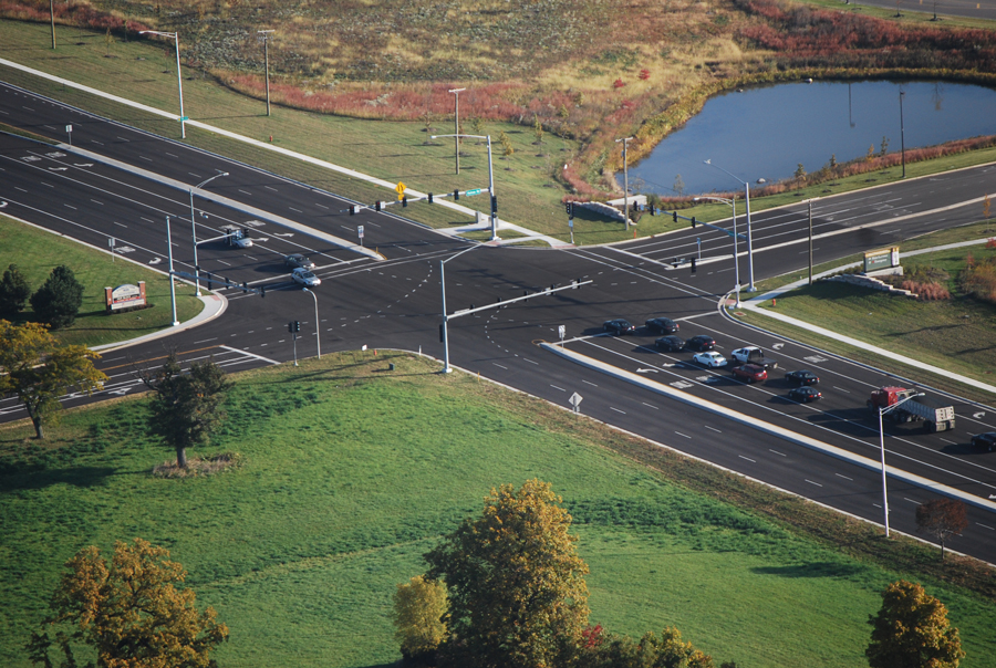 Sherman-Hospital-2 Aerial view of a modern intersection with traffic lights, vehicles, and green landscaping, showcasing infrastructure development.