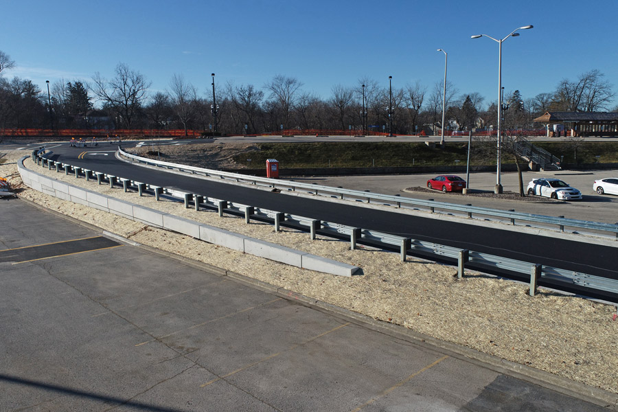 Barr-Metra-DJI_0001 Completed curved road with newly laid asphalt, guardrails, and roadside landscaping amid ongoing municipal improvements.