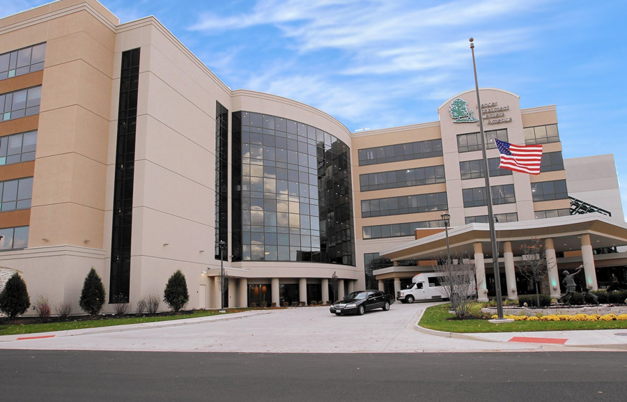 CTCA-IMG Modern healthcare facility featuring a large glass facade, landscaped entrance, and flagpole with the American flag in front.