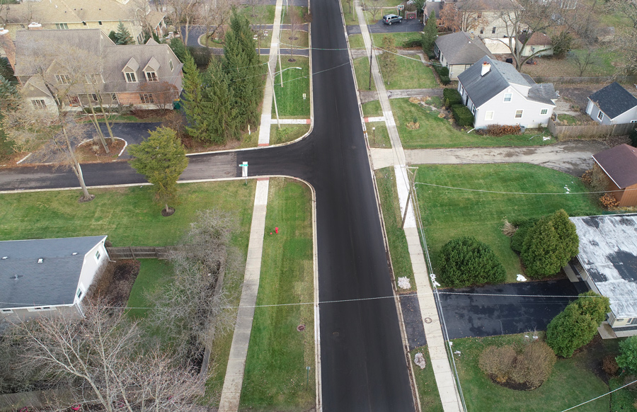 DF-Greenwood-DJI_0027 Aerial view of a residential street with freshly paved asphalt, sidewalks, and adjacent landscaped lawns in a suburban neighborhood.
