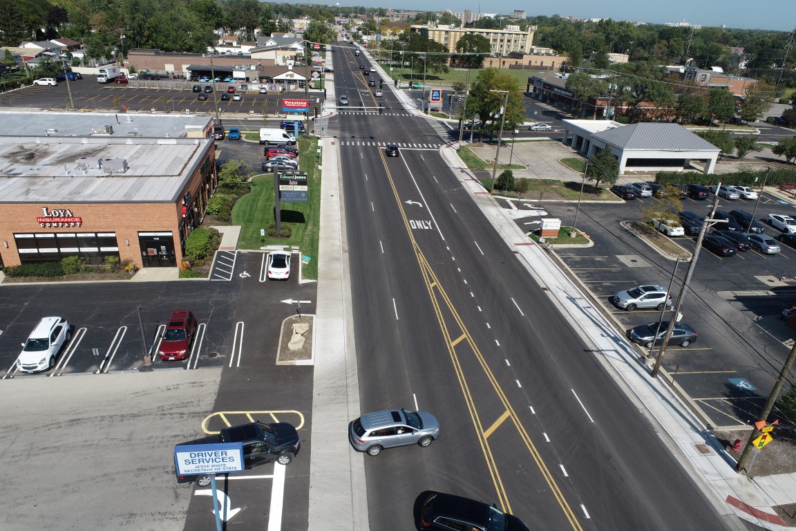 DCIM100MEDIADJI_0102.JPG Aerial view of a busy roadway featuring multiple lanes, vehicle traffic, and adjacent retail establishments, showcasing urban infrastructure.