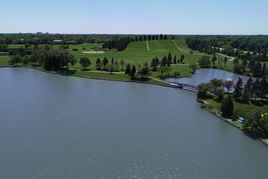 LakeShermerville-DJI_0002 Aerial view of a serene park featuring a lake, green hills, and walking paths, with trees lining the shoreline.