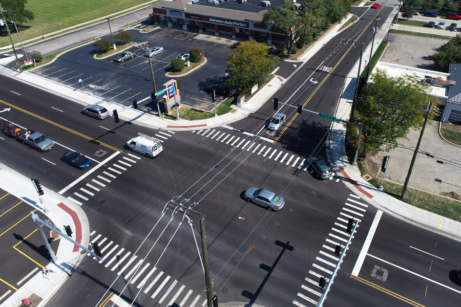 Lee-Forest-DJI_0149 Aerial view of a busy urban intersection featuring clear marked lanes, crosswalks, and nearby commercial buildings.