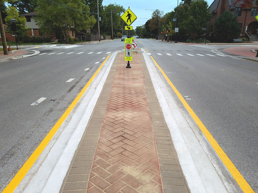 20201006_113735-Web Crosswalk with pedestrian signs and a brick-paved median on a suburban street, featuring clear road markings and landscaping.