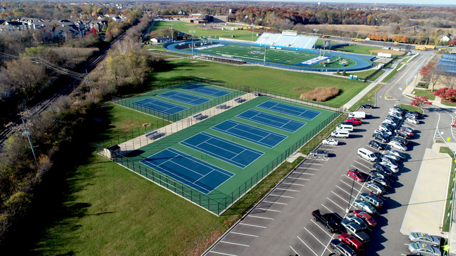 DJI_0027-Web Aerial view of a sports complex featuring tennis courts, a track, parking lot, and surrounding green space.