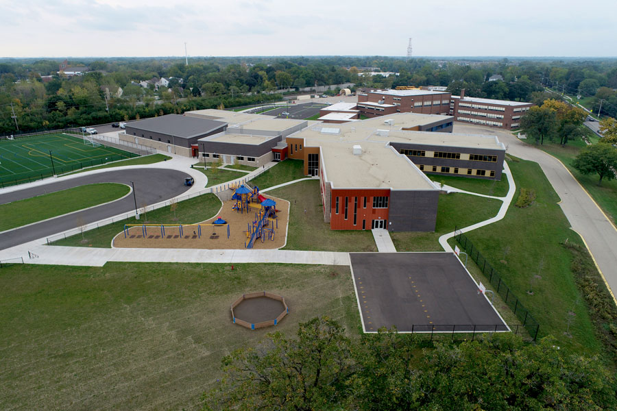 DJI_0120-Web Overview of a modern school campus featuring a playground, sports field, and landscaped areas with pathways and parking.