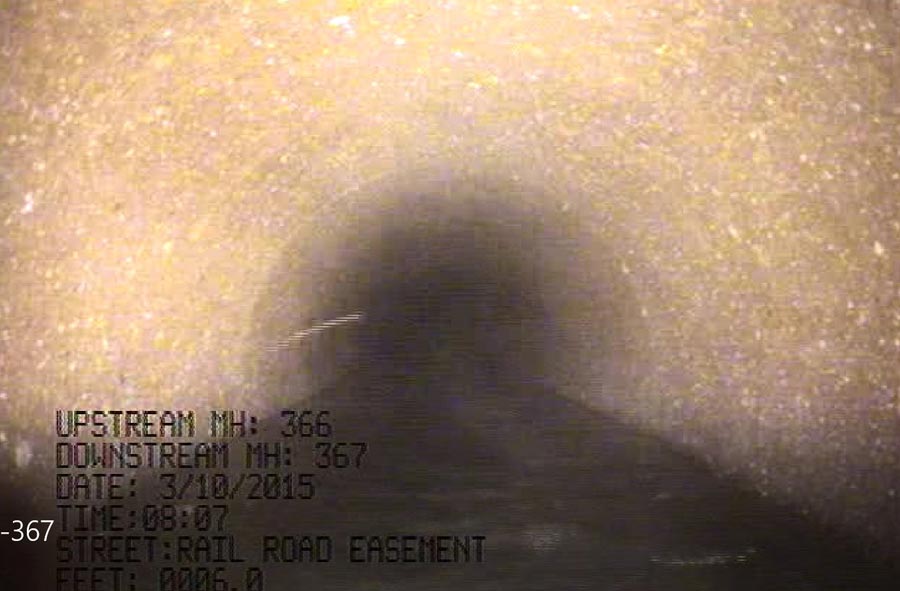 Barr-Sewer-2023-02-21-195554_web A shadowy view inside a sewer pipe, showcasing the interior structure with visible sediment accumulation.