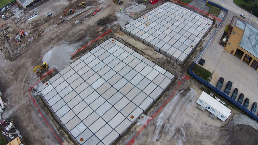CommunityIceCtr-DJI_00894_web Aerial view of a construction site featuring large concrete pads surrounded by machinery and gravel for future development.