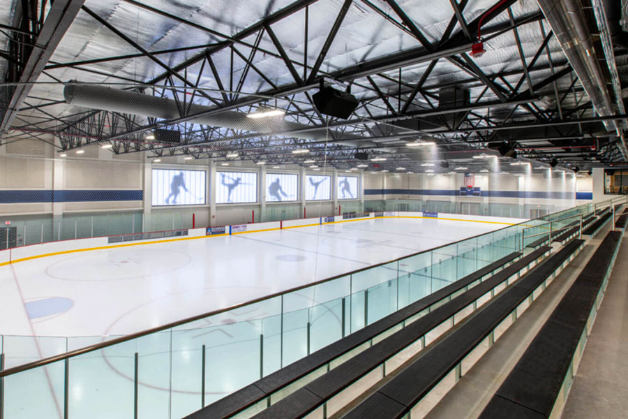 CommunityIceCtr-promopic_web An indoor ice hockey rink featuring a clear rink surface, seating areas, and large windows showcasing ice skating visuals.