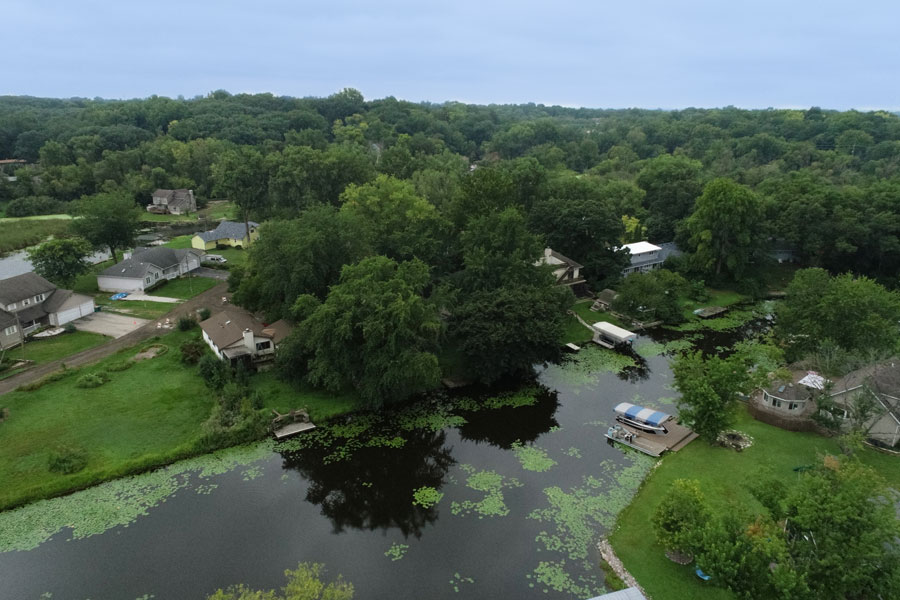 Knollwood-DJI_0216_web Aerial view of a residential area with homes bordering a serene lake, surrounded by lush greenery and lily pads.