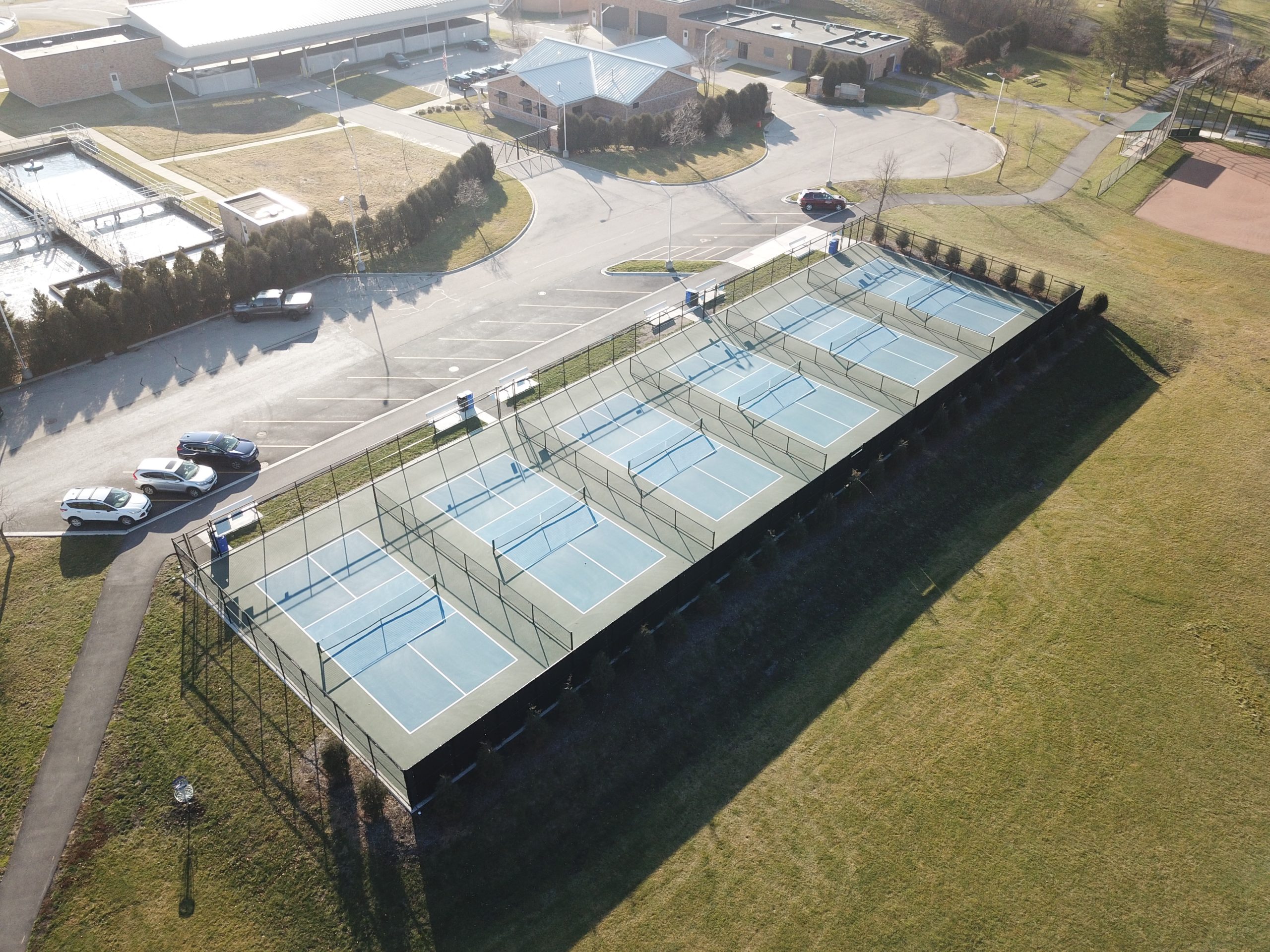 DCIM100MEDIADJI_0056.JPG Aerial view of newly constructed tennis courts, surrounded by green grass and parking spaces, showcasing urban recreational development.