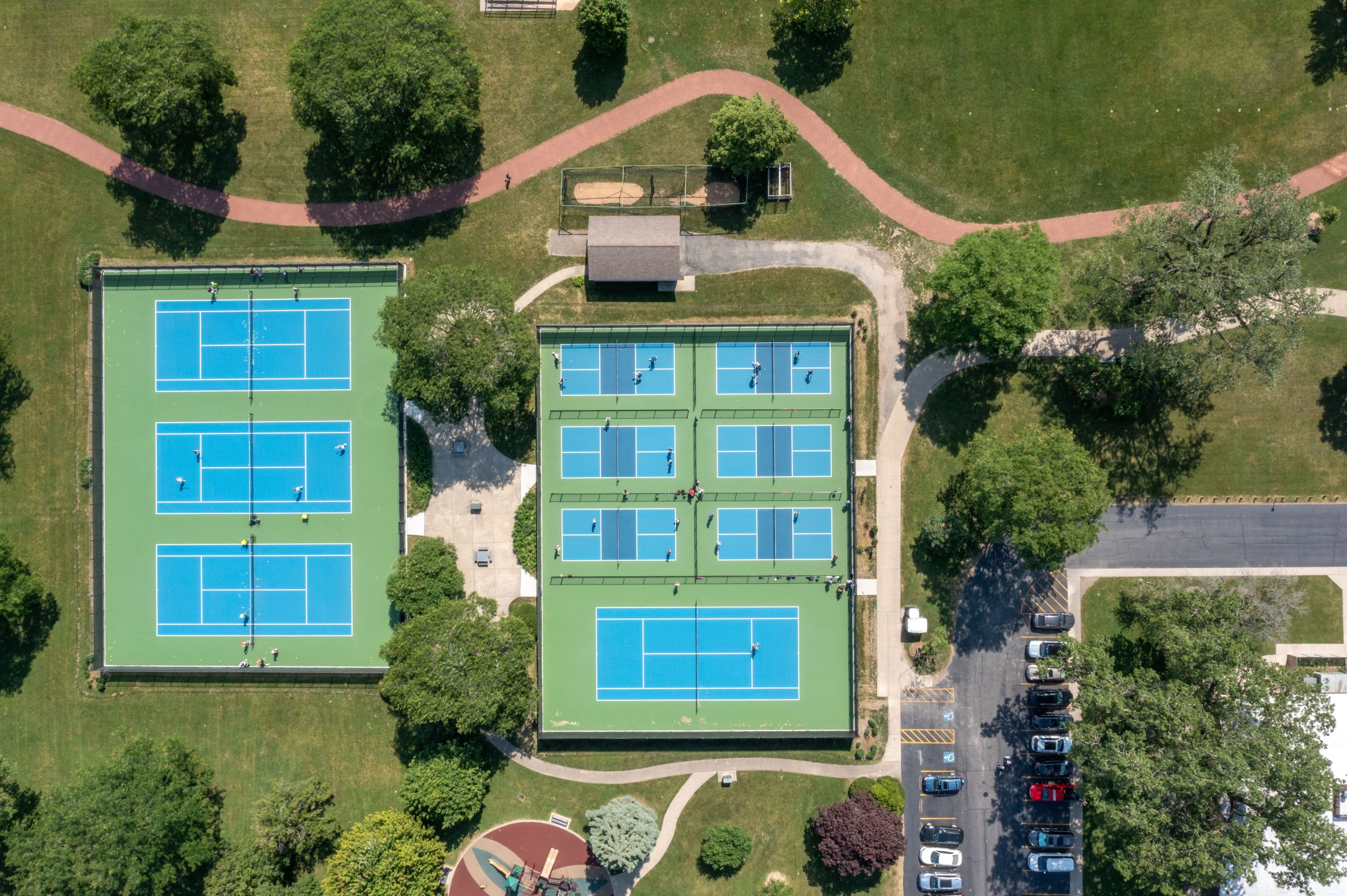 DJI_0436 Aerial view of a recreational park featuring multiple tennis courts surrounded by green areas and paved walkways.