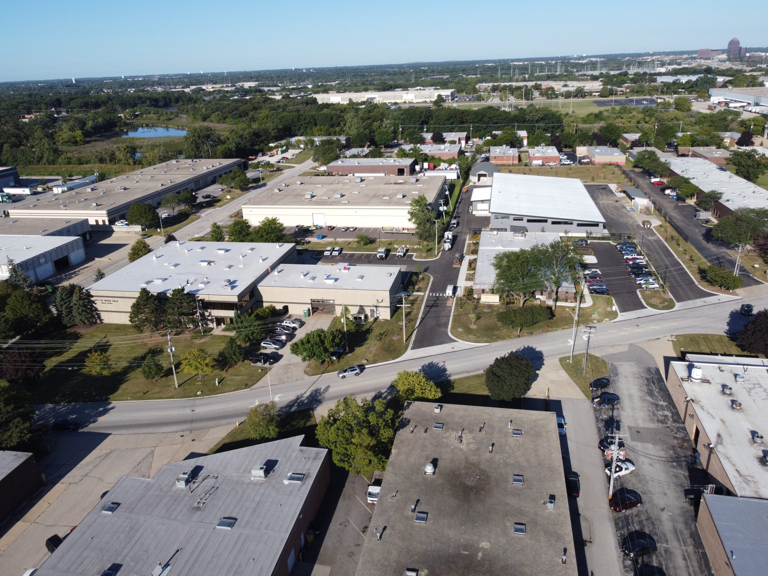 DCIM101MEDIADJI_0158.JPG Aerial view of a commercial area showcasing industrial buildings, parking lots, and surrounding greenery.