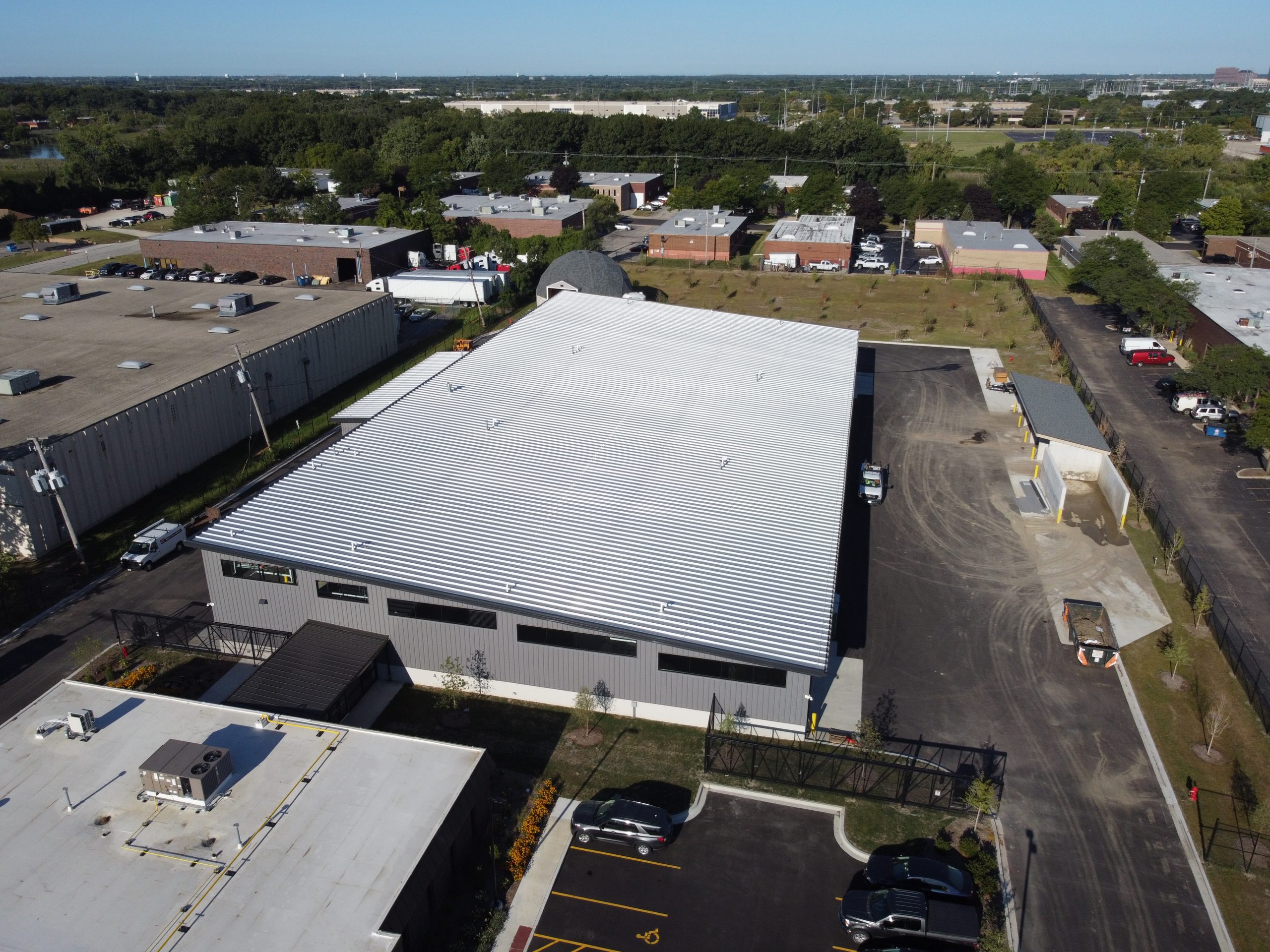 DCIM101MEDIADJI_0235.JPG Aerial view of a modern commercial building with a metal roof, surrounded by parking lots and landscaped areas.