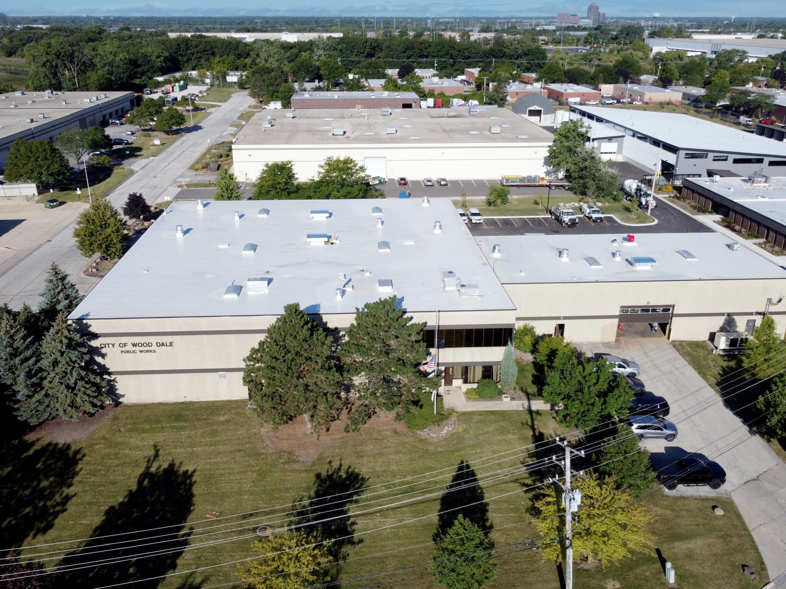 DJI_0263 Copy Aerial view of a municipal building in Wood Dale, surrounded by parking lots and landscaped green spaces.