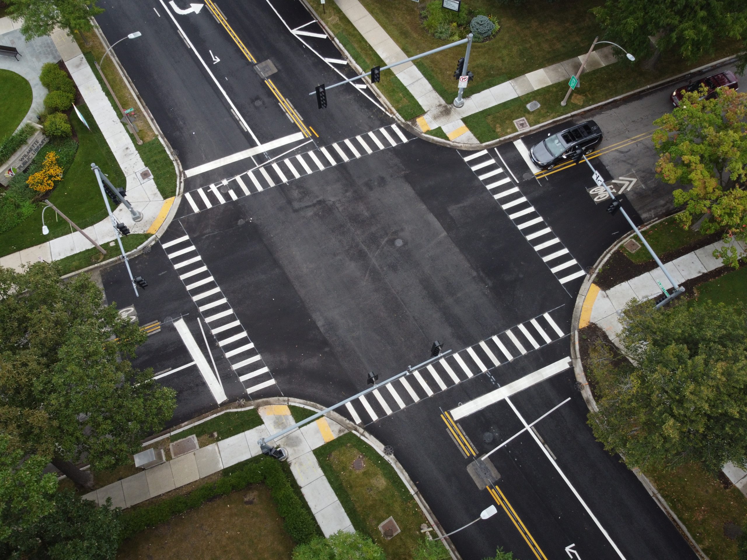 DCIM101MEDIADJI_0656.JPG Aerial view of a well-marked intersection with crosswalks and traffic signals, surrounded by greenery and landscaping.