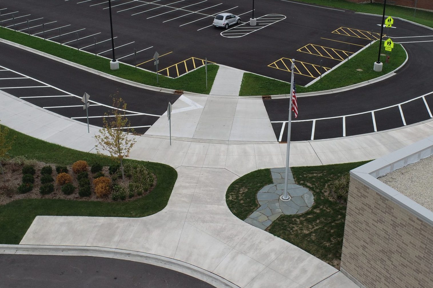 DCIM100MEDIADJI_0142.JPG Aerial view of a pedestrian pathway intersecting a parking lot, with decorative landscaping and a flagpole visible.