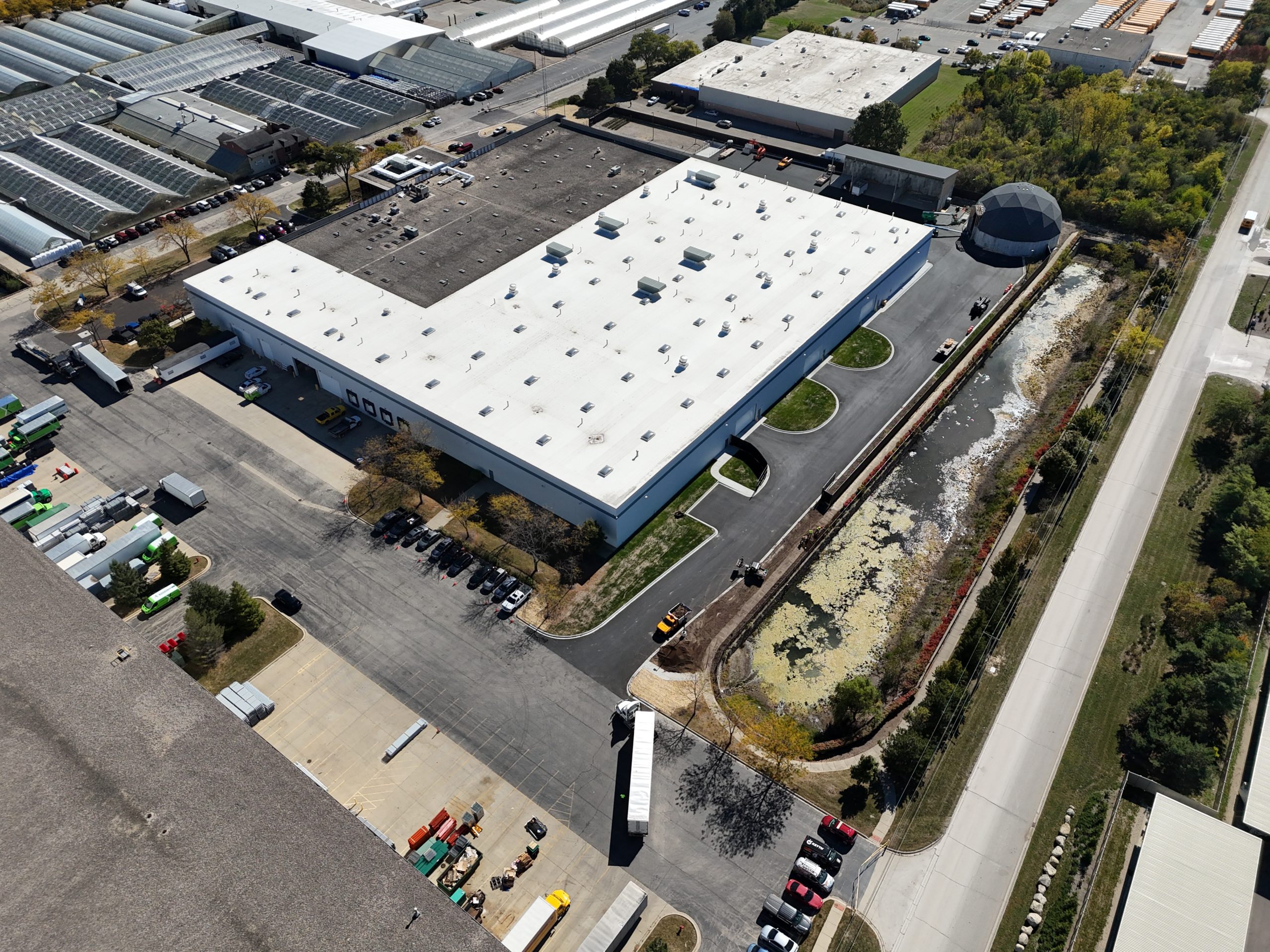 default Aerial view of a large commercial building surrounded by a paved lot, storage trucks, and a constructed wetland area.