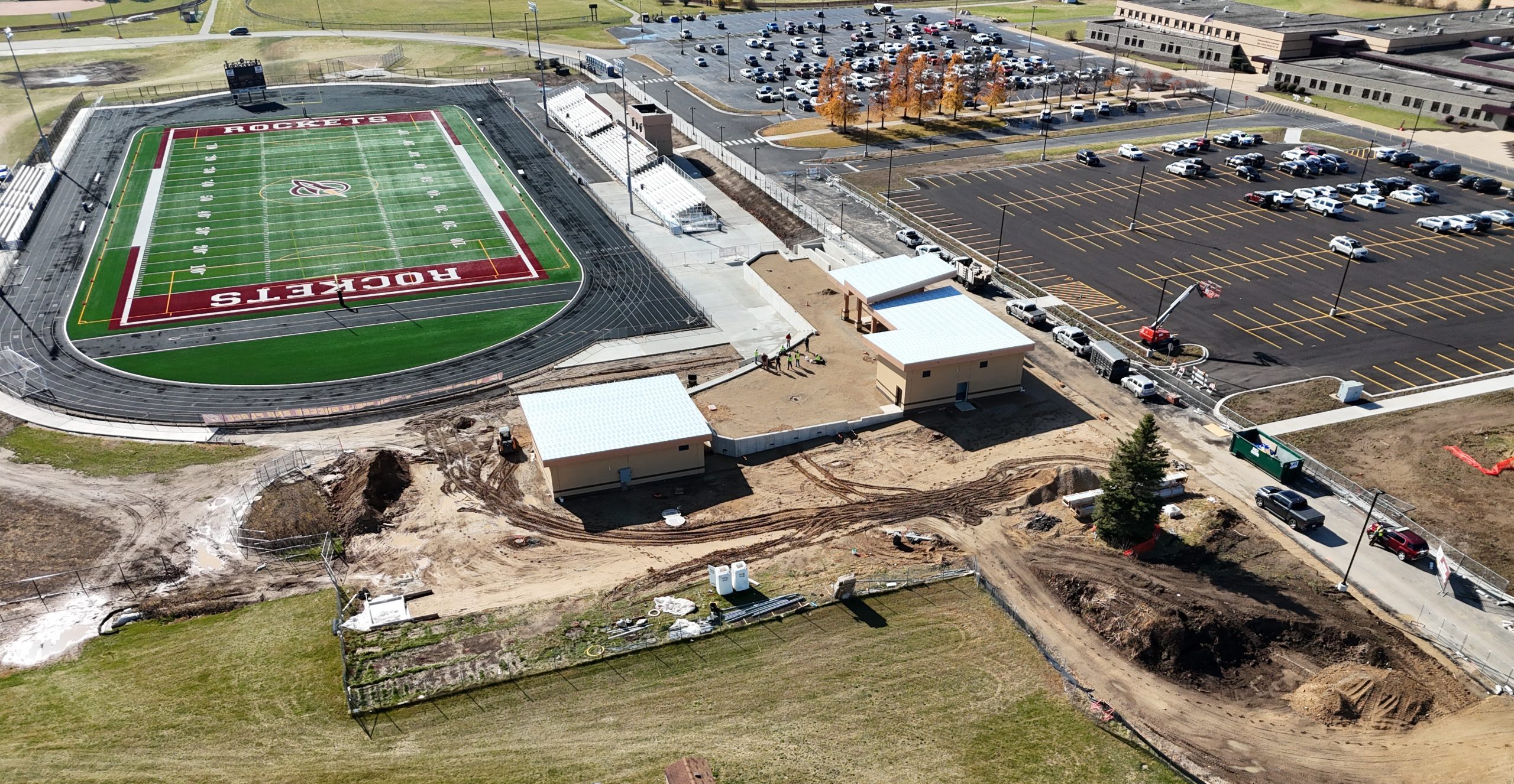 Aerial view of a sports field with adjacent construction site, featuring new building foundations and ongoing site excavation work.