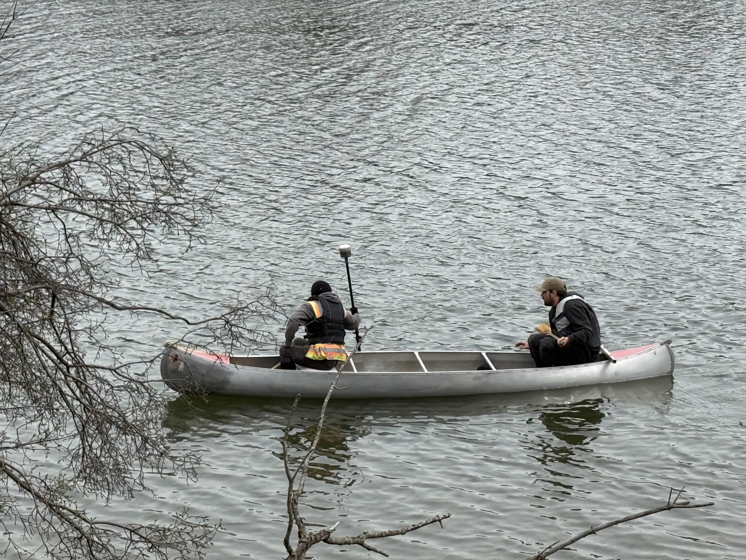 IMG_0119 Two professionals in a canoe conducting surveys on a body of water, surrounded by trees and natural scenery.