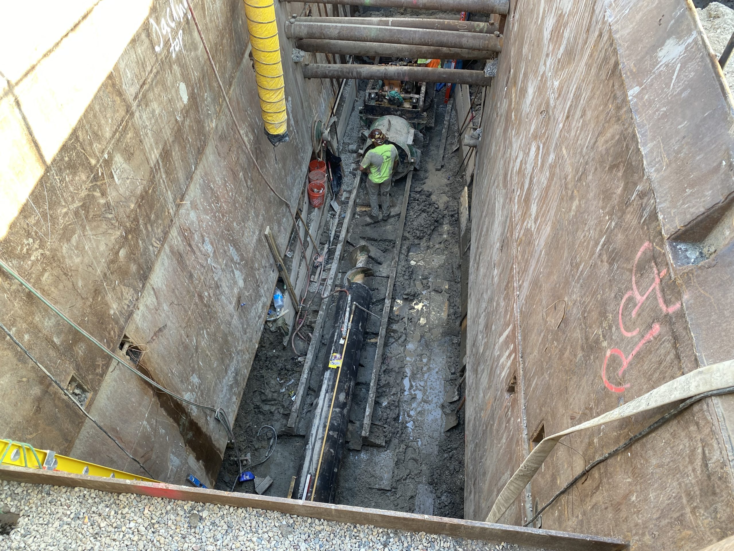 IMG_9160 Construction site showing deep excavation with workers and equipment in a trench, surrounded by wooden shoring for safety.