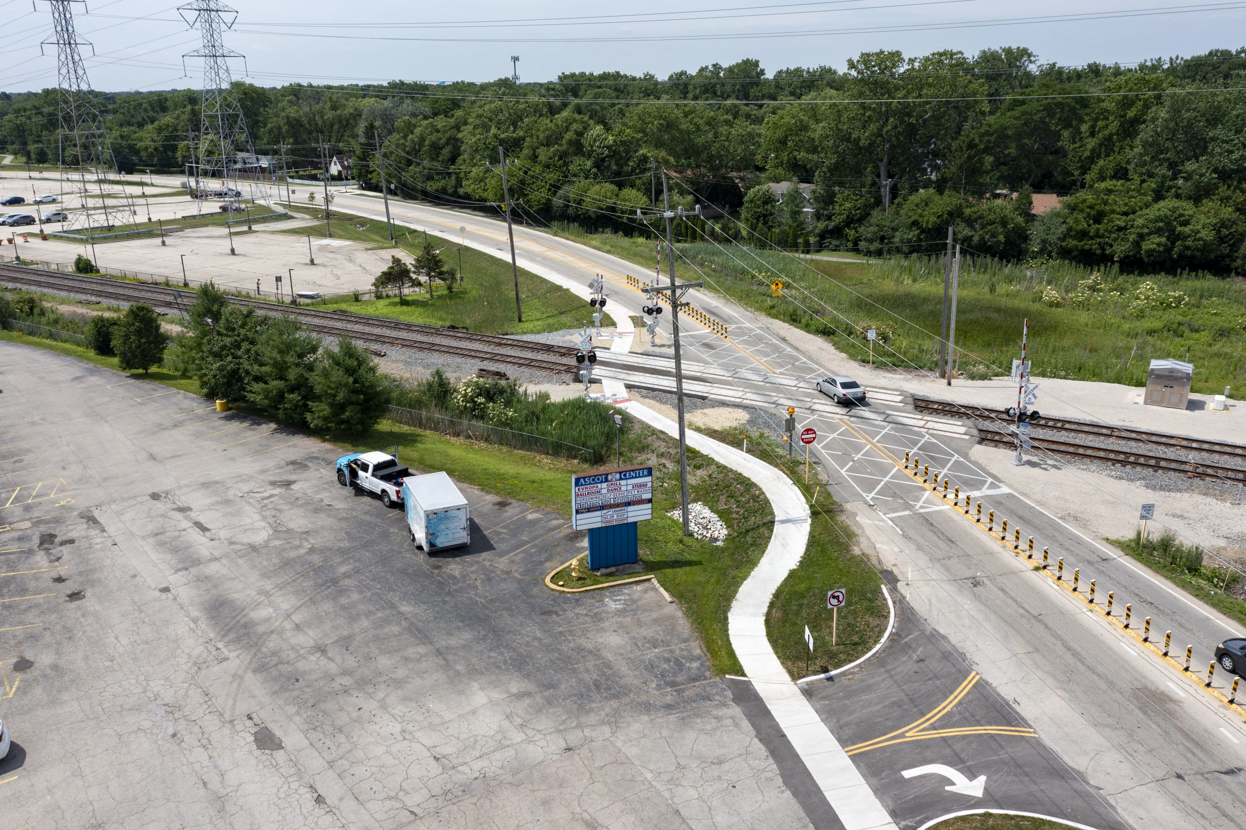 Wolf Rd-8 Aerial view of a railway crossing with traffic and construction elements, including a parking lot and newly marked roadways.