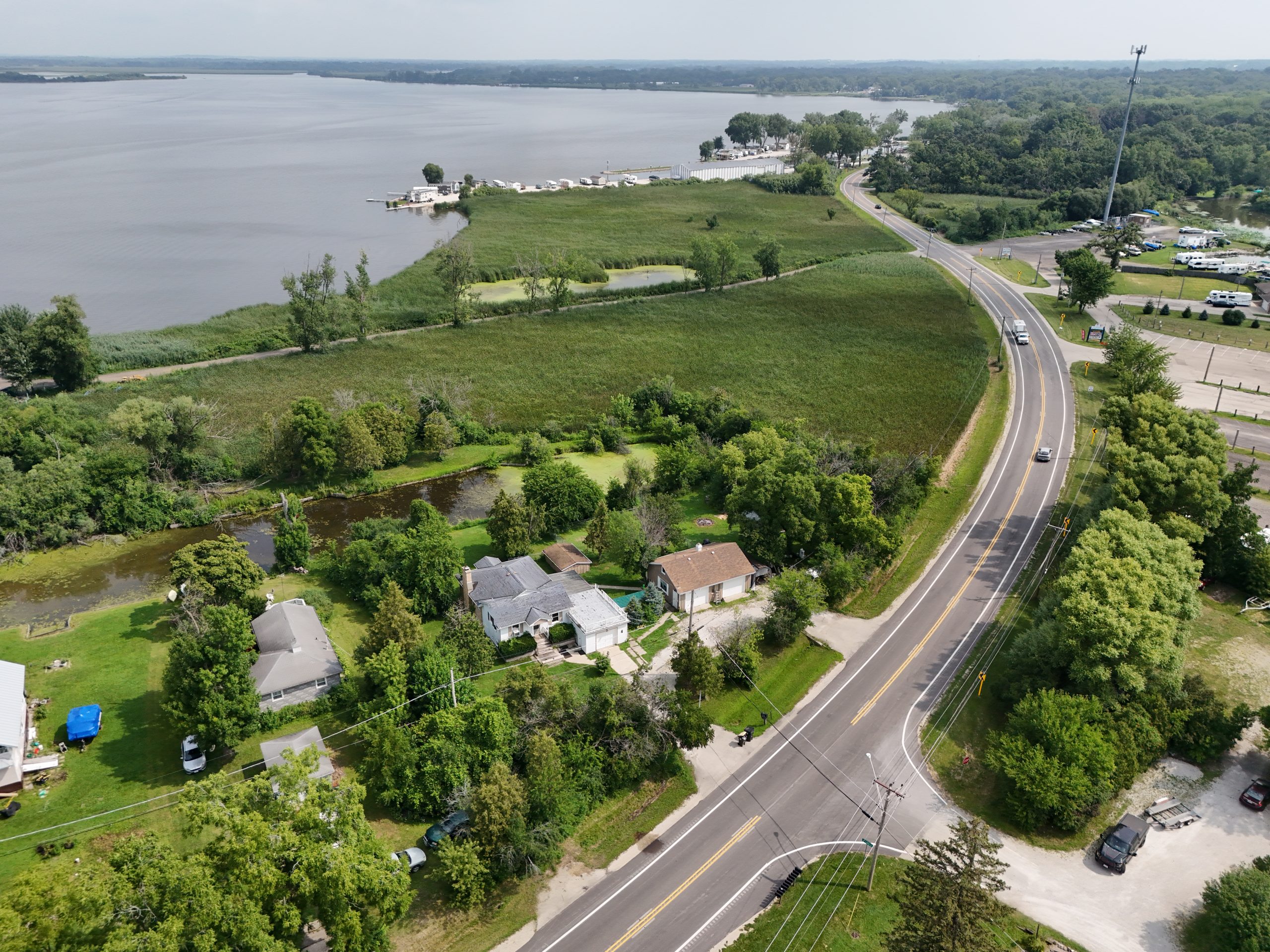 default Aerial view of a rural area with a winding road, houses, green fields, and a lake in the background, showcasing developed and natural landscapes.