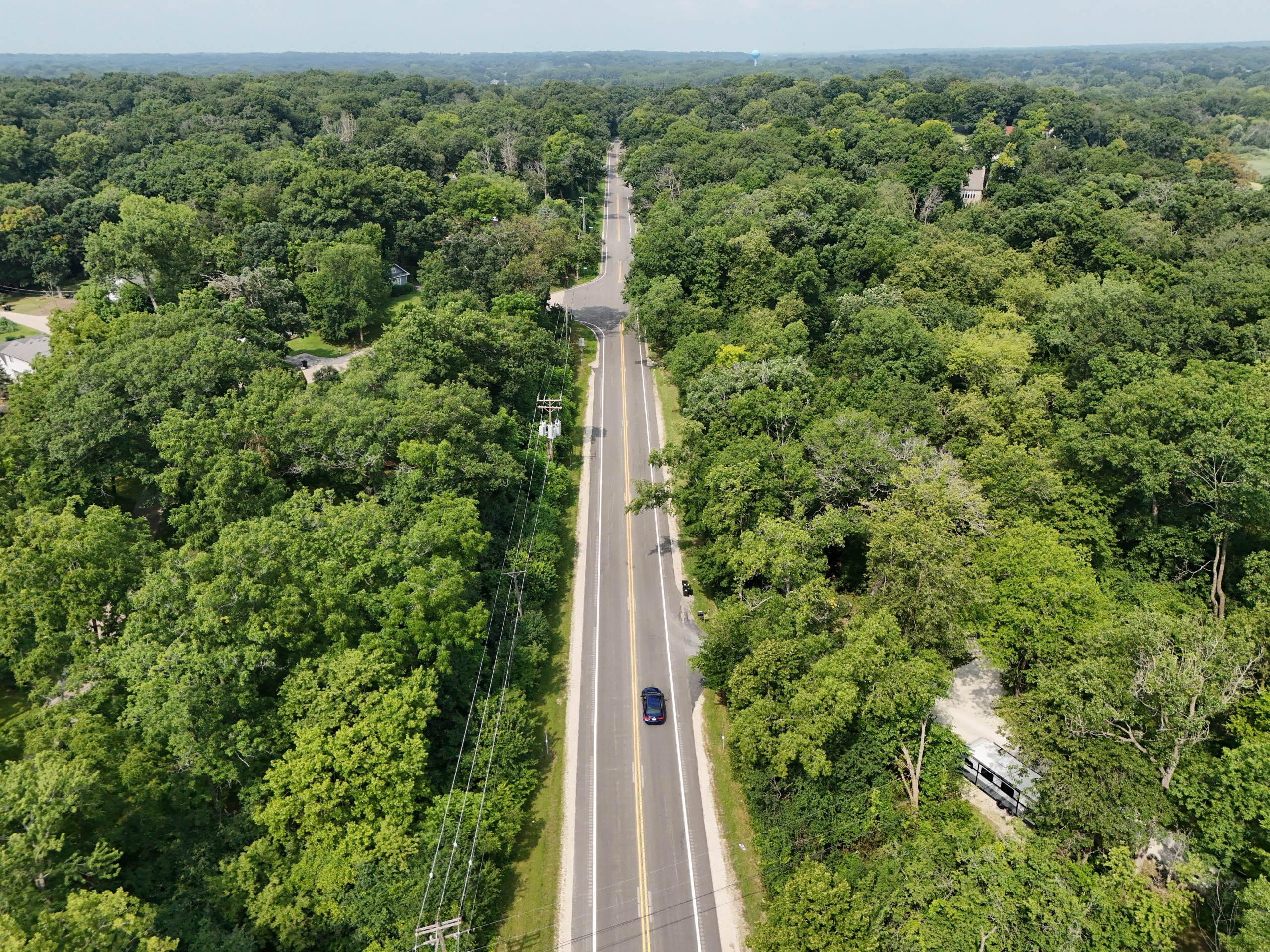 default Aerial view of a winding road surrounded by dense greenery and trees, showcasing municipal infrastructure and landscape integration.