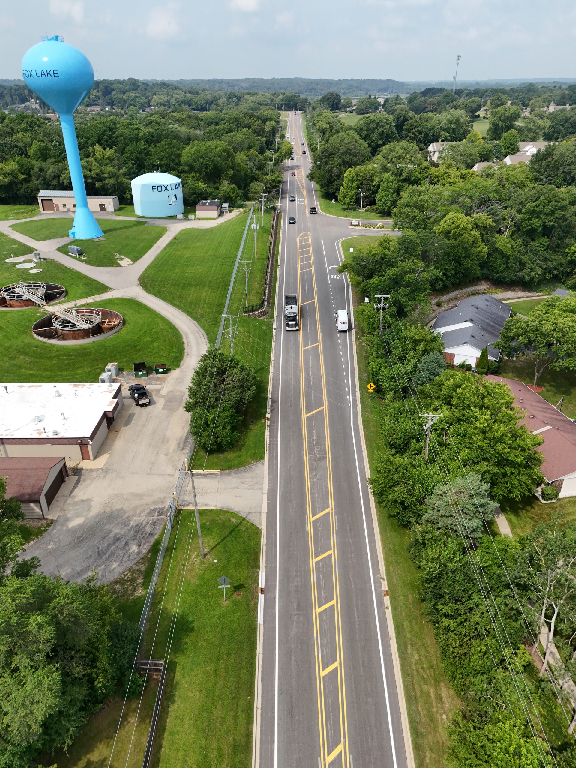 default Aerial view of a well-maintained roadway in Fox Lake, showcasing a water tower, green spaces, and nearby municipal buildings.
