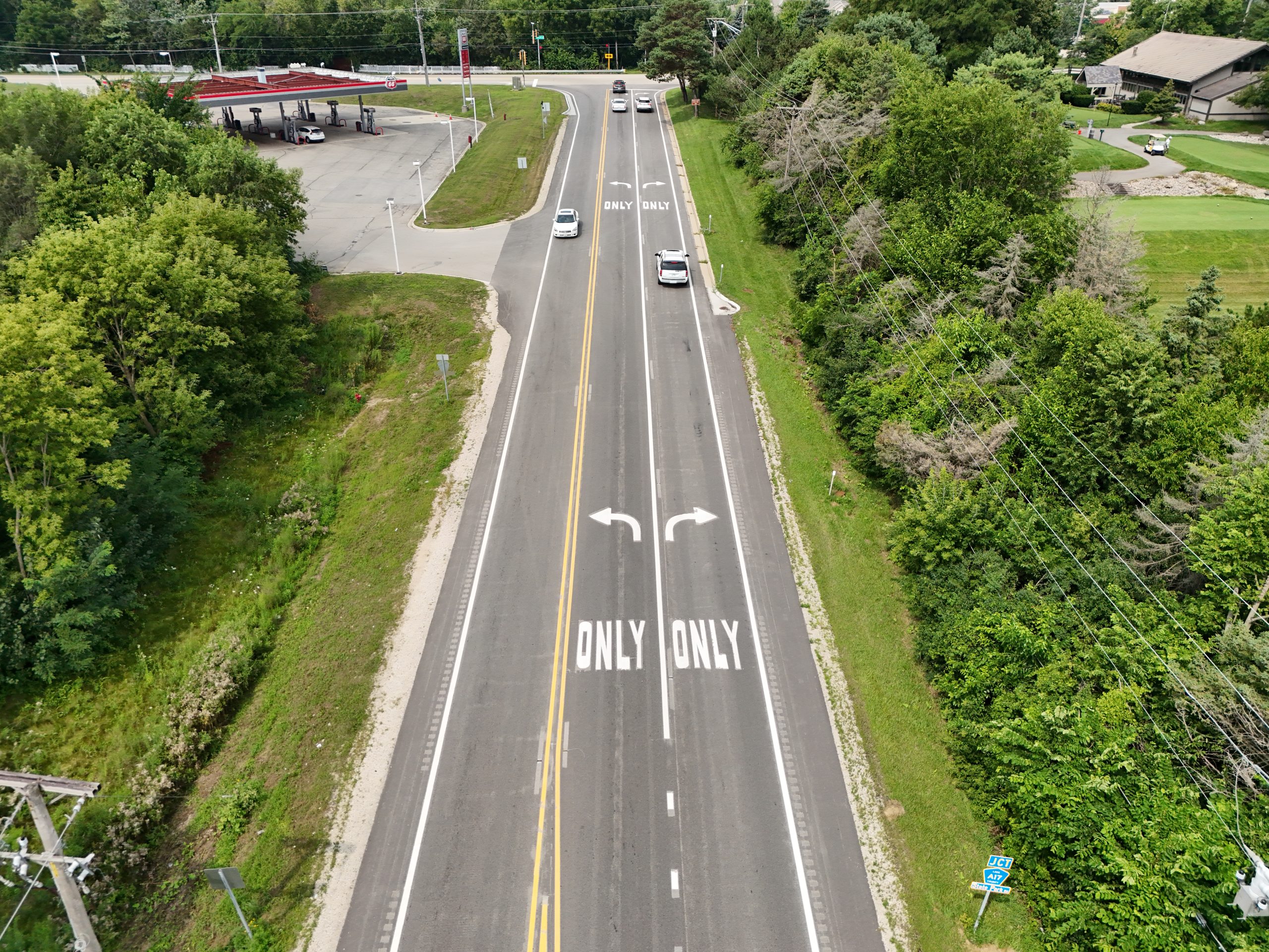 default Aerial view of a divided road with clear markings indicating lane directions, surrounded by greenery and adjacent commercial properties.