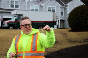 A civil engineer in a bright safety vest holds a key while overseeing construction at a residential site with parked vehicles in the background.