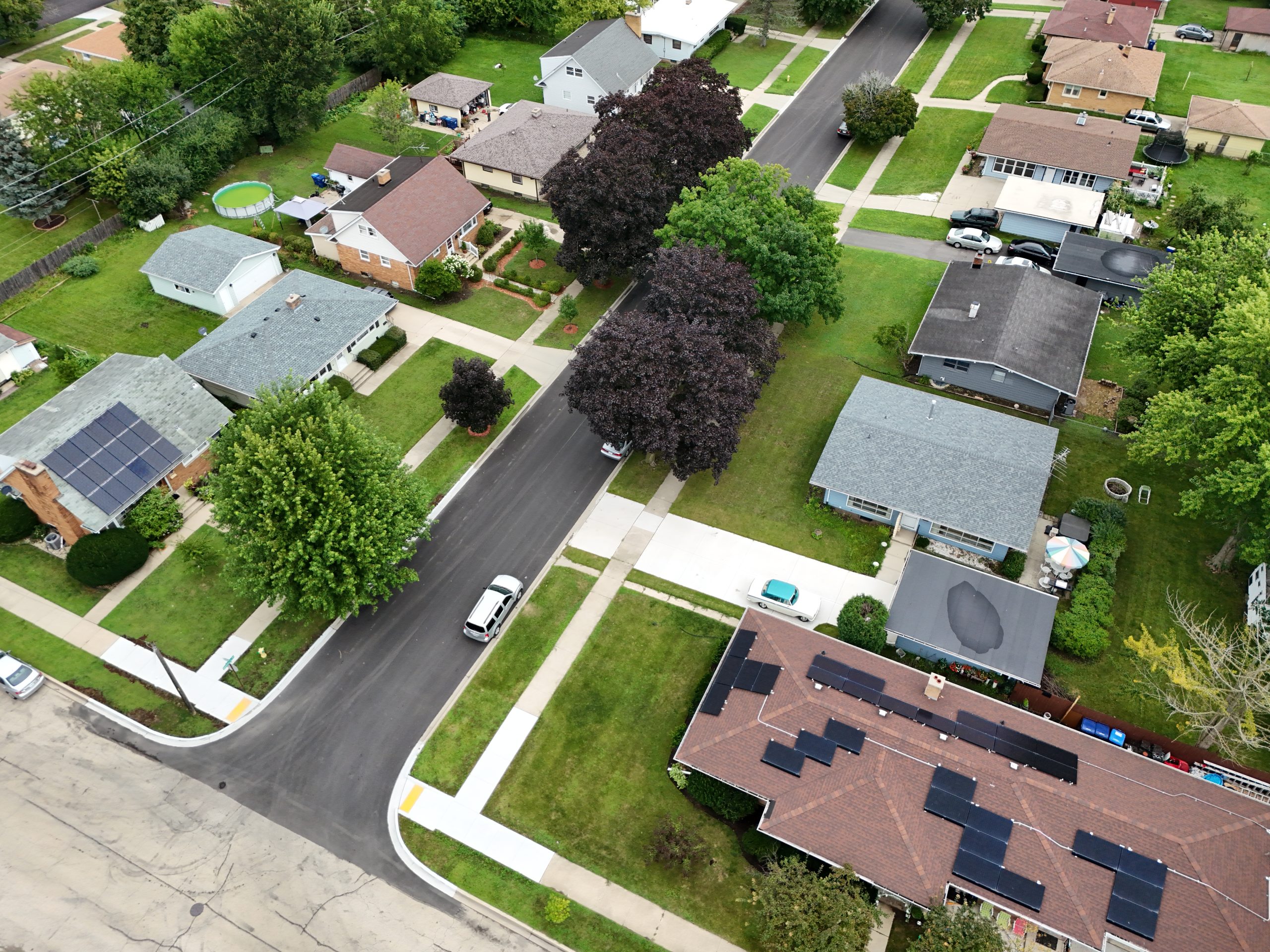 default Aerial view of a suburban neighborhood featuring residential homes with varied rooftops, sidewalks, and green spaces.