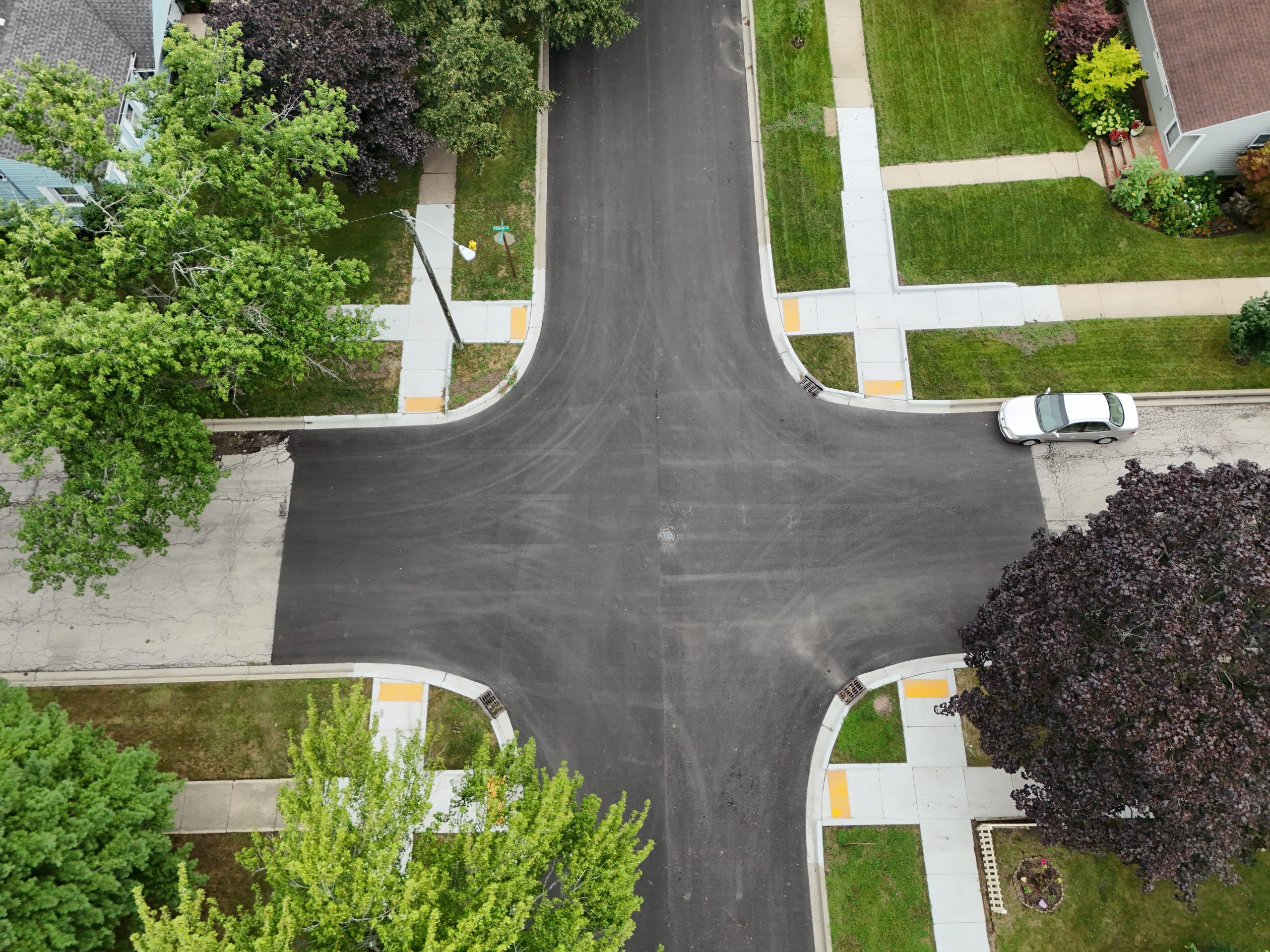 default Aerial view of a residential intersection featuring newly paved roads, sidewalks, and surrounding trees.