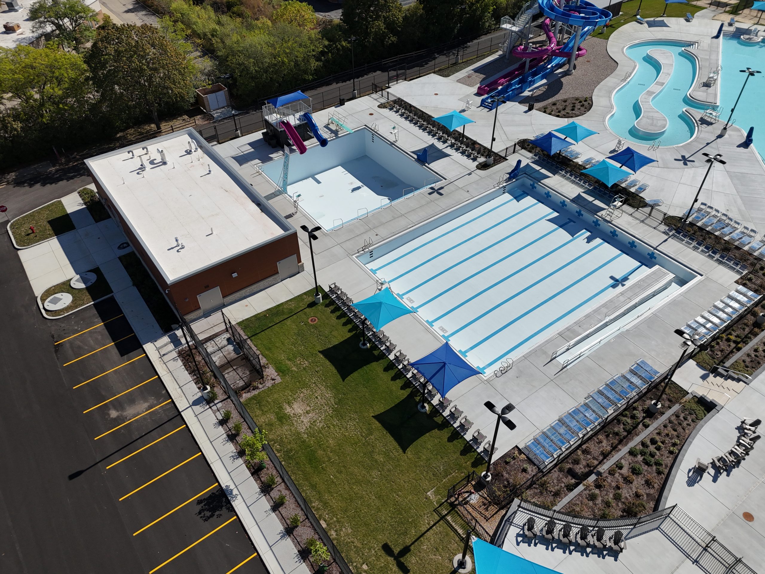 default Aerial view of a modern swimming pool complex featuring multiple pools, water slides, and shaded seating areas.