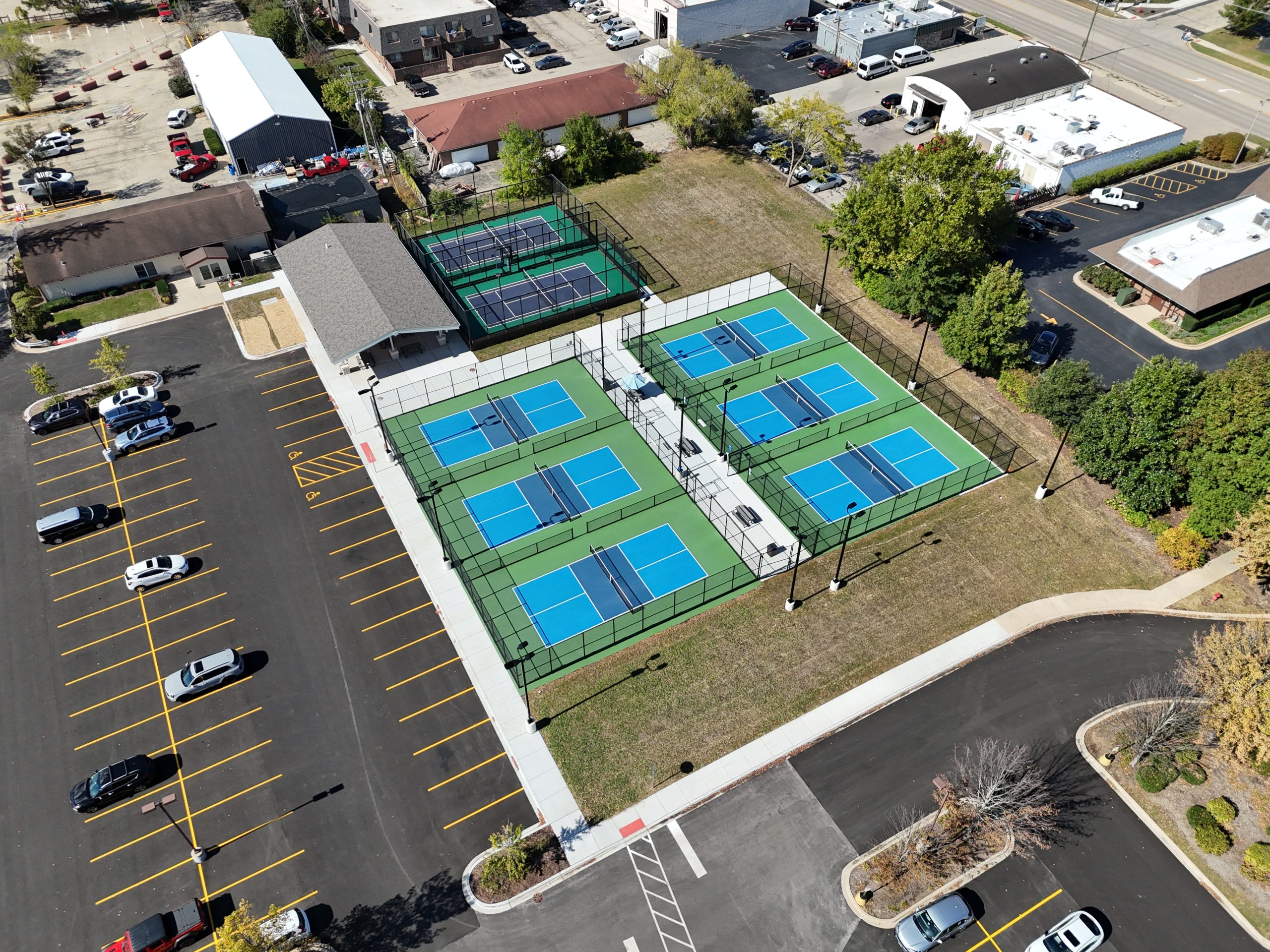 default Aerial view of newly constructed tennis courts surrounded by a parking lot, featuring multiple courts with bright blue surfaces and green fencing.