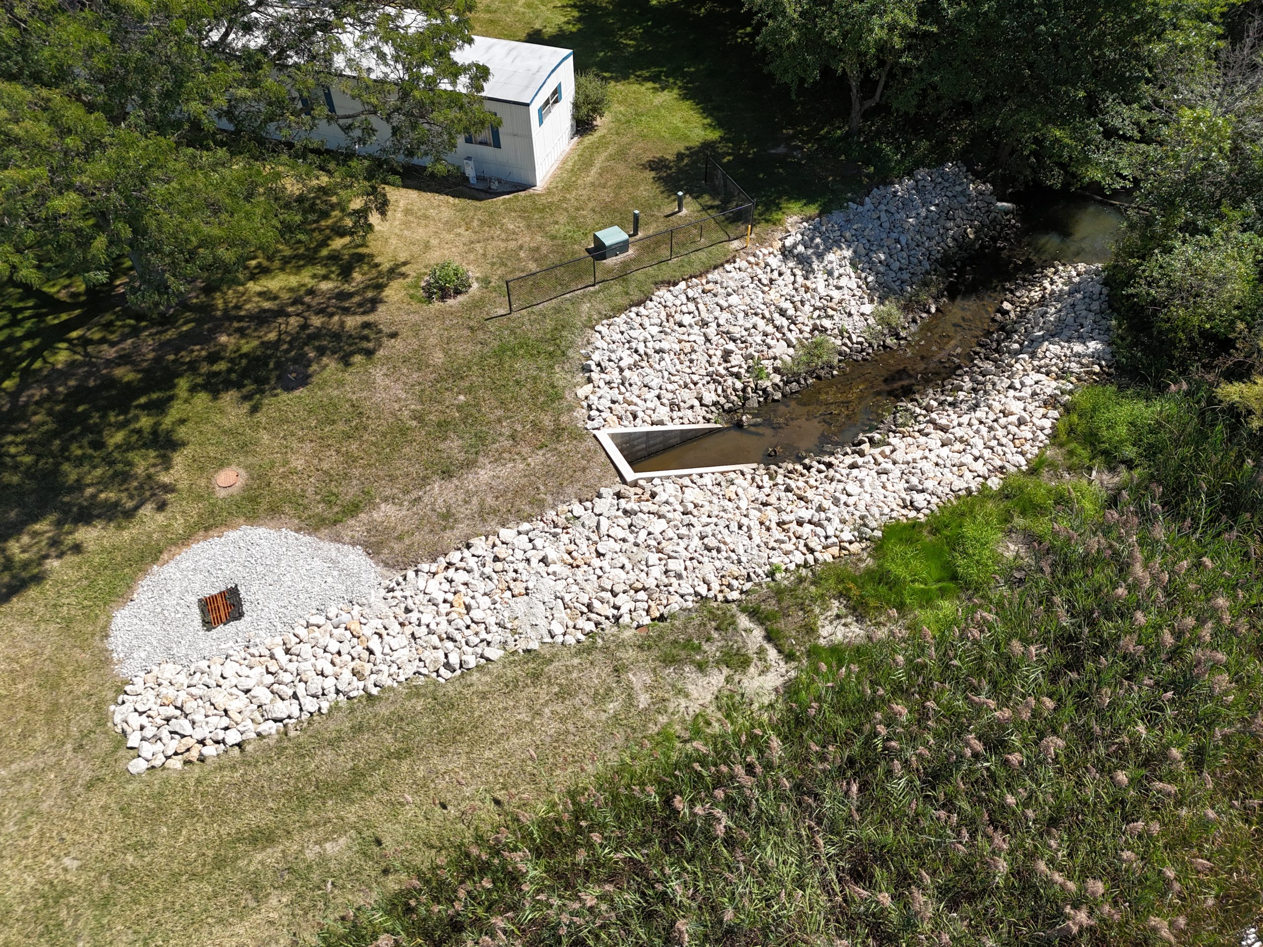 default A dry creek bed featuring rock riprap, designed for stormwater management, alongside a maintenance building in a landscaped area.
