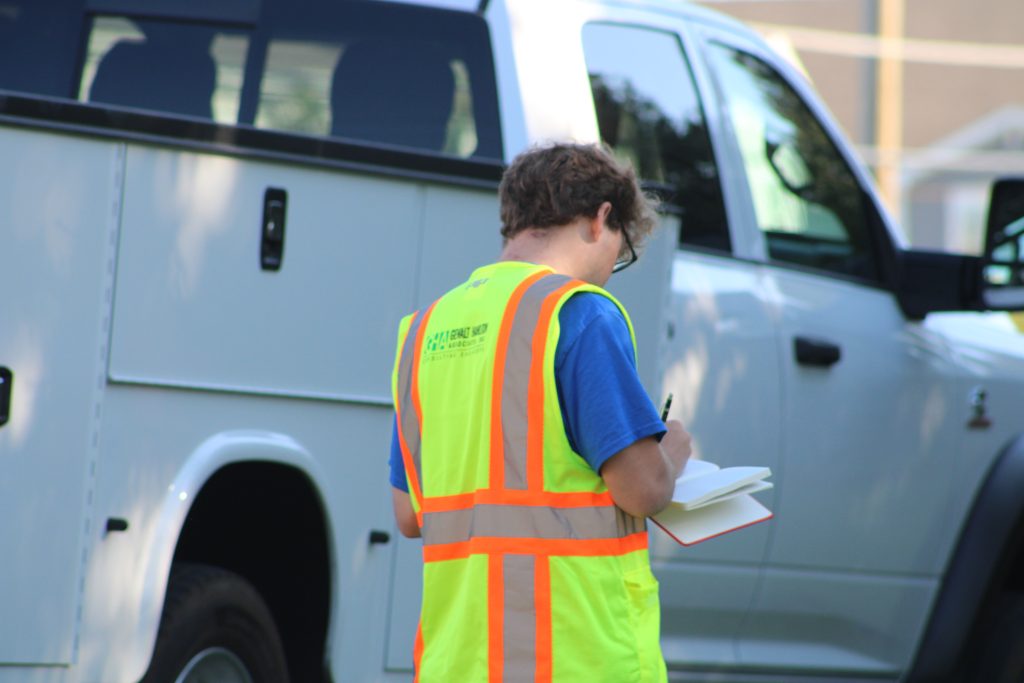 A GHA engineer wearing a safety vest records field notes next to a service truck at a project site